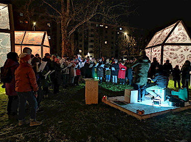 Die Sängerinnen und Sänger stehen vor den leuchtenden Häuschen der Kunstinstallation. Die Sängerinnen und Sänger stehen vor den leuchtenden Häuschen der Kunstinstallation.