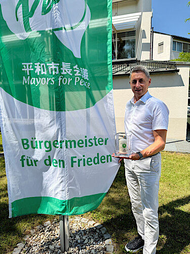Christoph Böck, Erster Bürgermeister von Unterschleißheim, mit der Friedenskerze vor der Flagge der Mayors for Peace