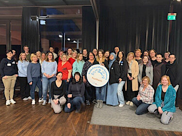 Gruppenbild mit ca. 30 Personen, in der Mitte wird ein Pappschild mit dem Logo der Kinderfreundlichen Kommune gehalten Gruppenbild mit ca. 30 Personen, in der Mitte wird ein Pappschild mit dem Logo der Kinderfreundlichen Kommune gehalten