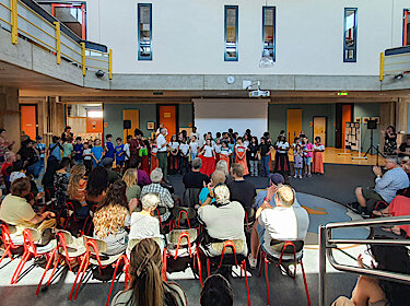 Im Vordergrund das Publikum, im Hintergrund Bürgermeister Seidl mit vielen Teilnehmerinnen und Teilnehmern bei der Aufführung in der Aula der Grundschule Süd