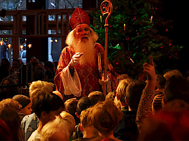 Nikolaus im Kostüm mit vielen Kindern vor einem Weihnachtsbaum